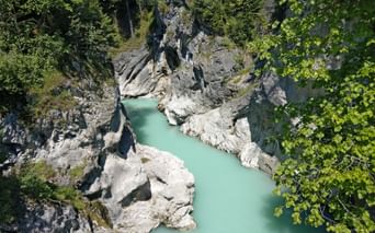 Luftaufnahme des türkisfarbenen Lech, der durch eine enge felsige Schlucht fließt, umgeben von dichtem grünen Wald und großen Kalksteinblöcken.