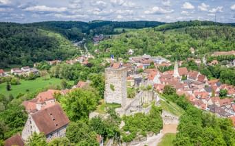Aerial view of Pappenheim in Altmühltal with medieval castle ruins, stone tower, and red-roofed houses nestled in green hills under blue sky.