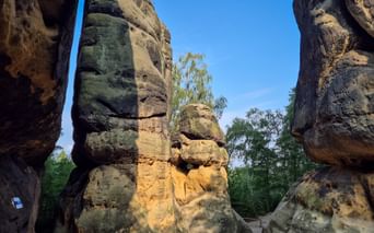 Blick durch enge Passage zwischen hohen Sandsteinfelsen am Schrammtor auf dem Malerweg, mit moosbewachsenen Oberflächen und blauem Himmel.