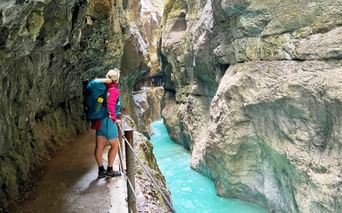 Wanderin mit Rucksack auf Holzsteg durch die Partnachklamm mit türkisfarbenem Wasser zwischen Kalksteinwänden.