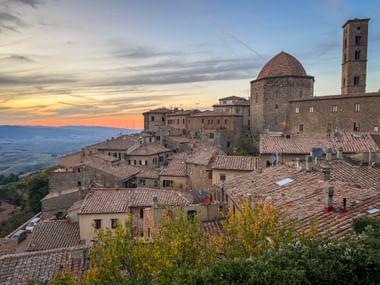 Historische Hügelstadt Volterra in der Toskana bei Sonnenuntergang mit Terrakottadächern, Steingebäuden, einer Kuppel und einem hohen Glockenturm.