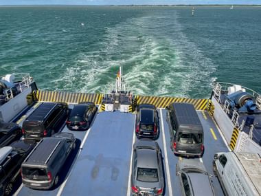 Blick vom Deck einer Autofähre in Westschweden mit parkenden Fahrzeugen in Reihen. Die Heckwelle zieht durch das türkisfarbene Wasser.