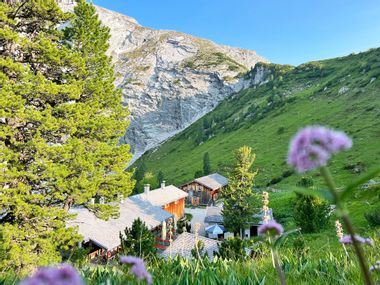 Das Schachenhaus mit Blumen im Vordergrund und steilen Wiesen und felsigen Berghängen im Hintergrund