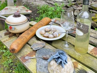 Rustikaler Tisch mit Topf, Baguette, Kartoffelteller, Weinglas, Flasche, Steinplatten und Tuch auf verwitterter Holzbank in Traben-Trarbach.