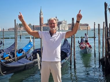 Walter Mirz with raised arms celebrating in Venice with gondolas and San Giorgio Maggiore church in the background.