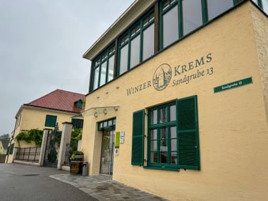 Yellow winery building with green shutters in Krems, Wachau. Sign reads 'Winzer Krems Sandgrube 13' on the facade.