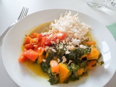 White plate with basmati rice and colorful vegetable curry containing spinach, carrots, tomatoes, and pumpkin in golden sauce.