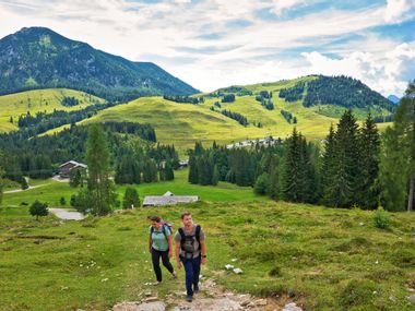 Junge Familie beim Wandern auf der Postalm mit Almhütten, Almwiesen und Bergen im Hintergrund