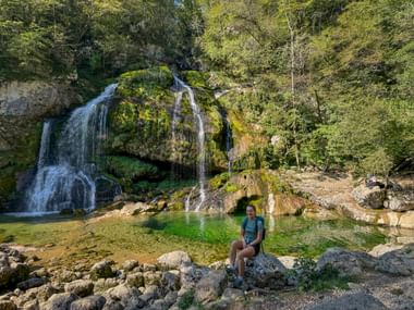 Wanderer rastet auf Felsen am Virje-Wasserfall in den Julischen Alpen. Moosbewachsene Felsen mit Wasserfällen und grünem Becken im Soča-Tal.