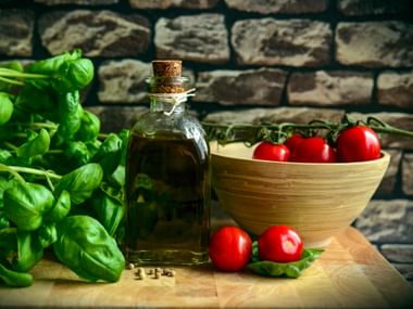 Frischer Basilikum, Olivenöl in einer Glasflasche, Tomaten in einer Holzschüssel