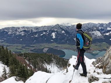 Wanderer am verschneiten Gipfel mit Blick auf den winterlichen Wolfgangsee