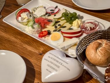 Traditional Austrian Heuriger platter with cheeses, cold cuts, boiled egg, grapes, vegetables, and bread rolls in a basket on a wooden table.
