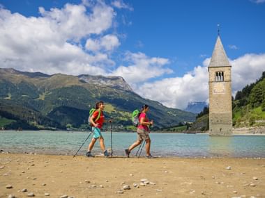 Hikers on the shore of Lake Reschen with a view of the church tower