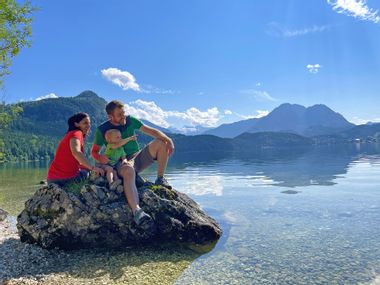 A family sits on a stone on the shore of Lake Altaussee