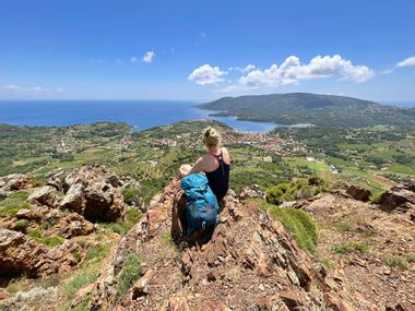 Wanderpause auf einem Felsvorsprung mit Blick auf eine darunterliegende Ortschaft und die Küste