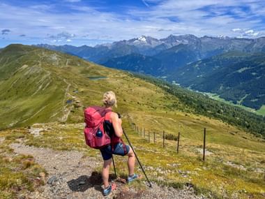 Wanderin mit pinkem Rucksack und Wanderstöcken auf Bergkamm im Gschnitztal, mit Blick auf Alpengipfel und grünes Tal.