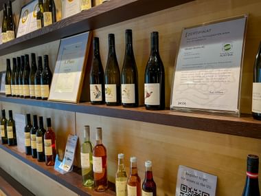 Wooden shelves displaying wine bottles from Krems winery. Top shelf shows four dark bottles and a framed Austrian wine certificate.
