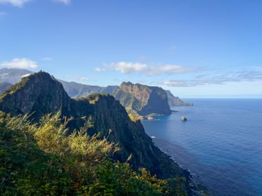 Dramatic coastal cliffs at Miradouro do Cabo de Larano on Madeira's north coast, with steep rocky peaks descending to the blue Atlantic Ocean.