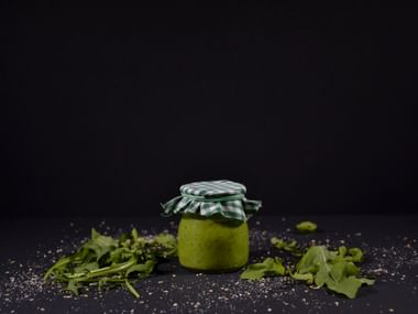 Glas mit grünem Pesto, Ruccola, grün-weißem Tuch