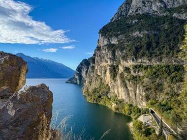 Panoramic view of Strada del Ponale path carved into steep cliffs above Lake Garda, with dramatic rock formations and blue water below.