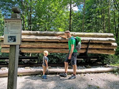 Wanderer mit Sohn vor Holzstämmen auf dem Bockerlbahnweg