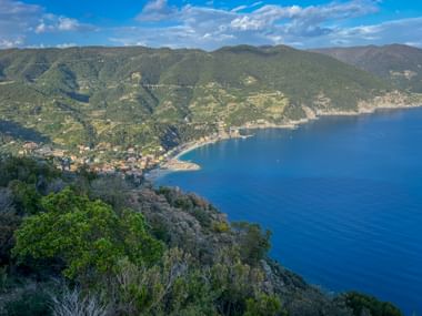 Panoramic view from Punta Mesco near Levanto showing the Ligurian coastline with green mountains, a bay, and blue Mediterranean Sea.