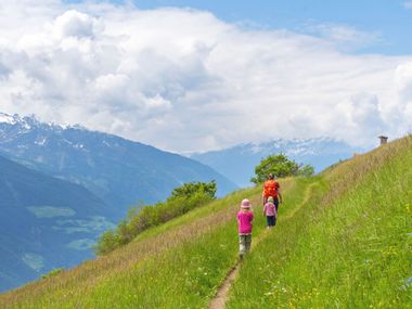 Frau mit zwei Kindern wandert durch Wiese mit Bergsicht