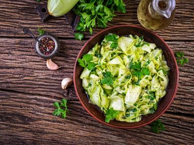 Salatschüssel mit Zucchini, Petersilie und Olivenöl auf der Seite