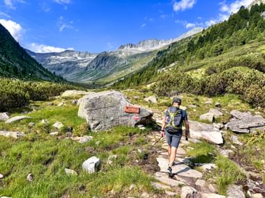 Wanderer mit Rucksack und Stöcken auf Bergweg in Hohe Tauern bei Krimml, mit Wegmarkierung auf Fels, grünem Tal und Alpengipfeln.