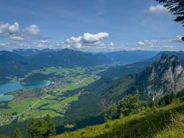 Aerial view from Bleckwand of Wolfgangsee lake surrounded by green valleys and mountains in Salzkammergut, with rocky cliffs in foreground.