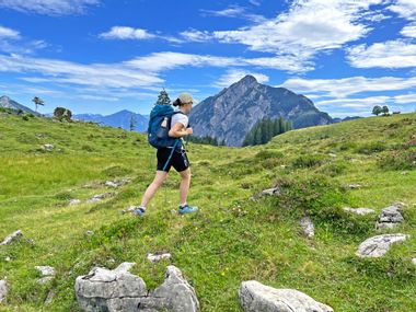 Hiker in the middle of an alpine landscape, mountains in the background, green meadows