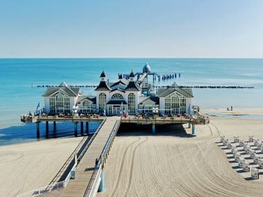 Weiße verzierte Seebrücke mit Türmen und Kuppeln in der Ostsee am Strand von Sellin auf Rügen, mit Sandstrand und blauem Wasser.