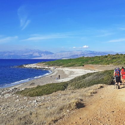 Hikers on the stony coast of Agia Ekaterin, mountain panorama in the background