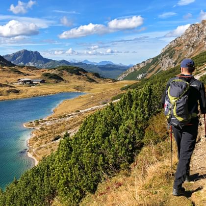 A hiker enjoys the panorama with a view of the alpine hut by the mountain lake
