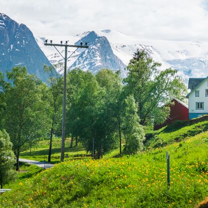 View of the Jostedalsbreen glacier with dandelion meadows and a typical white wooden house in the foreground