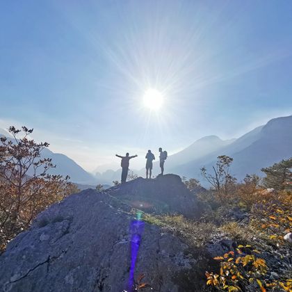 Three hikers in the sunshine on the mountain, one person has his arms outstretched, autumnal nature