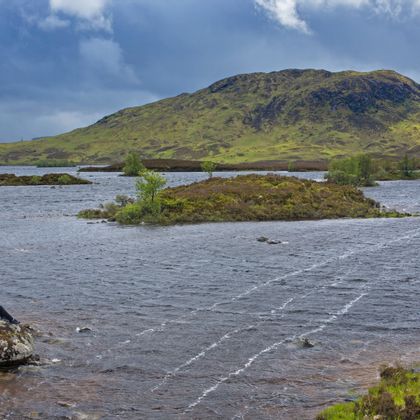 Woman walker sitting on a large stone on the shore of a windswept loch of Rannoch Moor