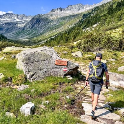 Wanderer mit Rucksack und Stöcken auf Bergweg im Krimmler Achental, Nationalpark Hohe Tauern. Wegmarkierung auf Felsen, Alpengipfel im Hintergrund.
