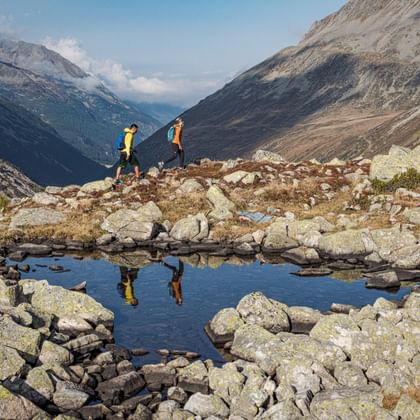Reflection of two hikers in a mountain lake with panorama