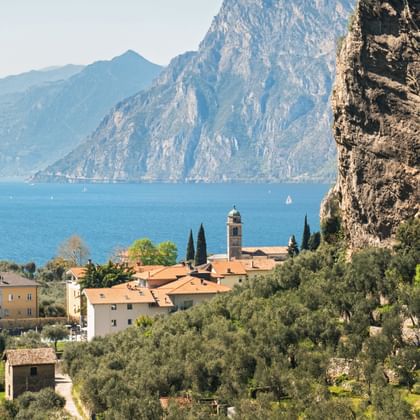 Torbole village with church tower nestled between dramatic cliffs and Lake Garda, surrounded by olive groves and cypress trees.
