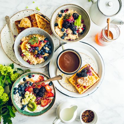 Table with various breakfast dishes, waffles, porridge with fruit, honey, milk