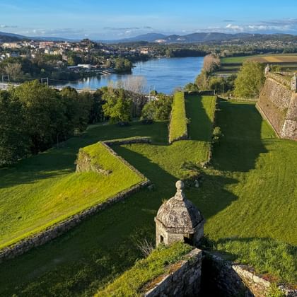 Luftaufnahme der Festung Valença mit Steinmauern und Wachturm, Blick auf Fluss mit Brücke und Stadt im Hintergrund unter blauem Himmel.