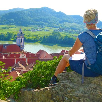 Wanderin bei einer Rast, sitzend auf einem Felsen oberhalb von Dürnstein und der Donau