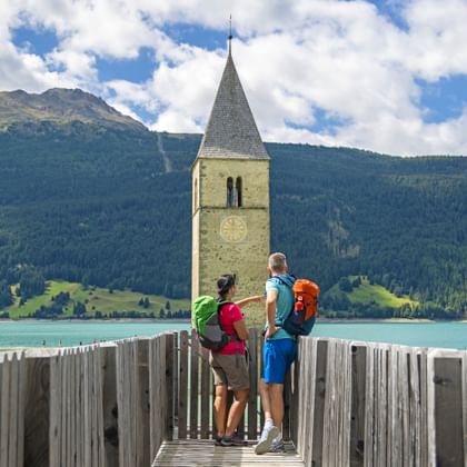 Wanderpaar genießt den Ausblick auf den versunkenen Kirchturm am Reschensee an der Via Claudia Augusta
