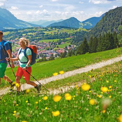 Hiking couple on panoramic path above Reit im Winkel with flower meadow in the foreground and mountains in the background