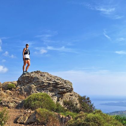 Woman stands in sportswear on a rock high above the sea, blue sky, sunshine