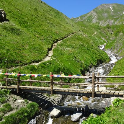 Narrow wooden bridge over a torrent with a view to the head of the valley on the hiking trail around Mont Blanc