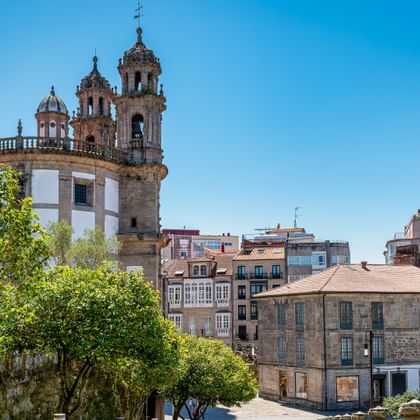 La Peregrina Kirche mit markanten Glockentürmen in Pontevedra, umgeben von Wohngebäuden und grünen Bäumen unter blauem Himmel.