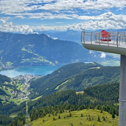 Elevated viewing platform on Schmittenhöhe with visitors overlooking Zell am See lake, green mountains, and valleys in the Kitzbühel Alps.