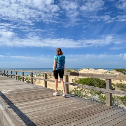 Wanderin wandert am Holzsteg entlang der Praia Verdelago am Meer